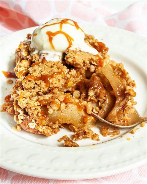 A scoop of apple crisp with flaky, crumbly topping, icecream, and a drizzle of caramel. Image from cravinghomecooked.com