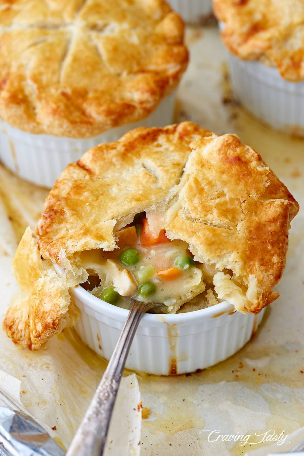 A homemade chicken pot pie with a flaky crust and creamy filling that has chicken, peas, carrots, and more all baked in a oven safe ceramic bowl. Image from cravingtasty.com