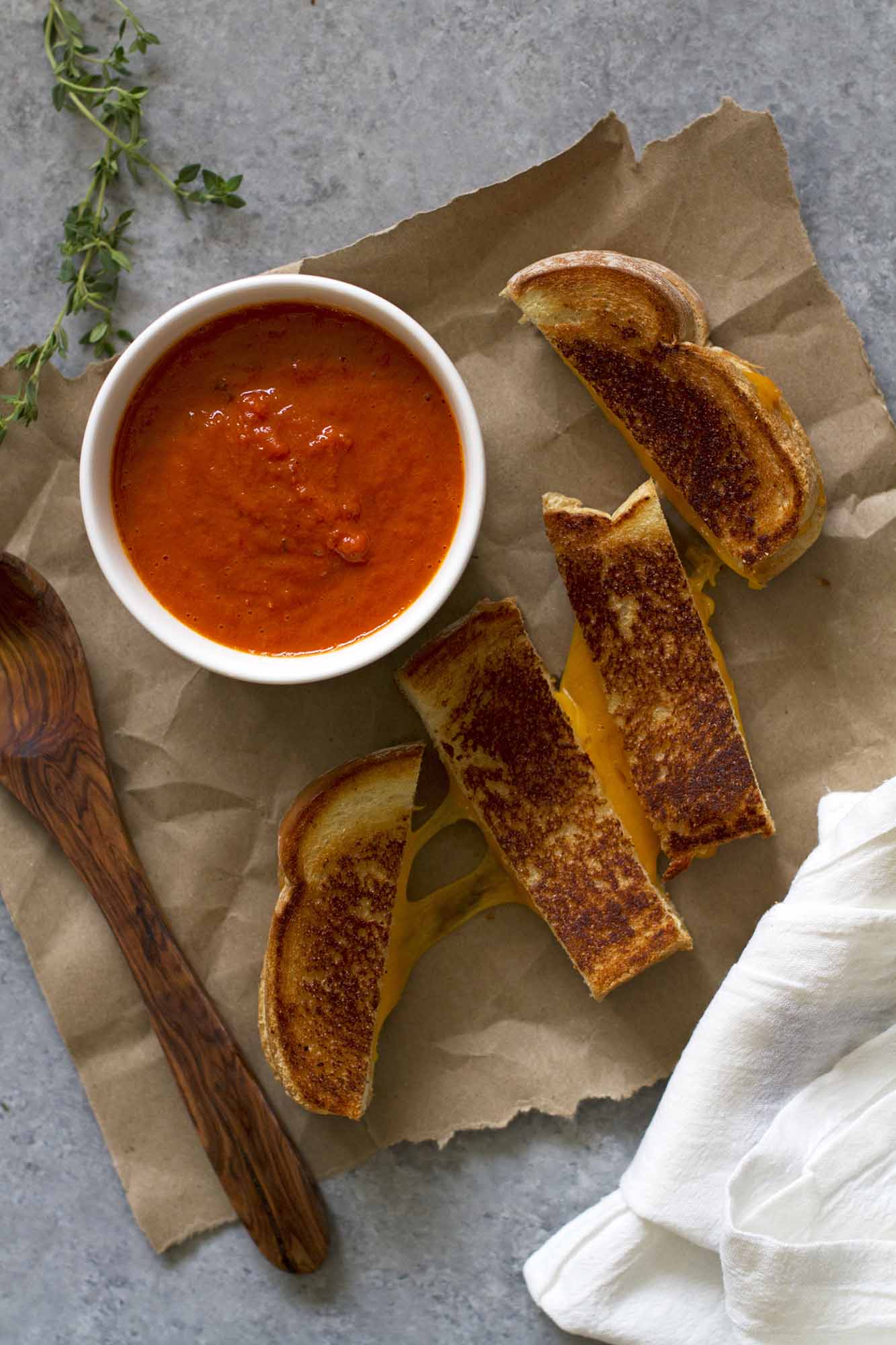 A bowl of deep red tomato soup next to a grilled cheese sandwich that has been cut into four vertical strips. Image from girlversusdough.com