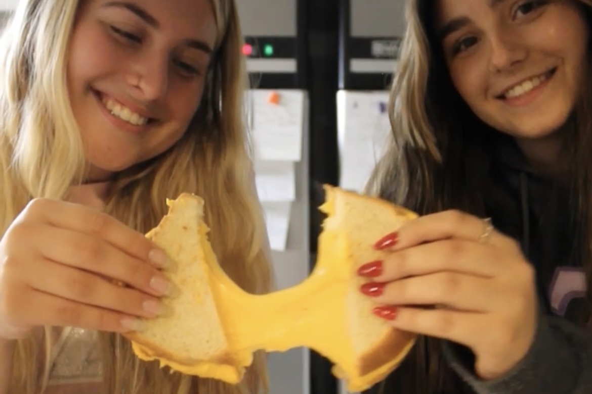 Two women holding a grilled cheese and smiling as they pull it apart